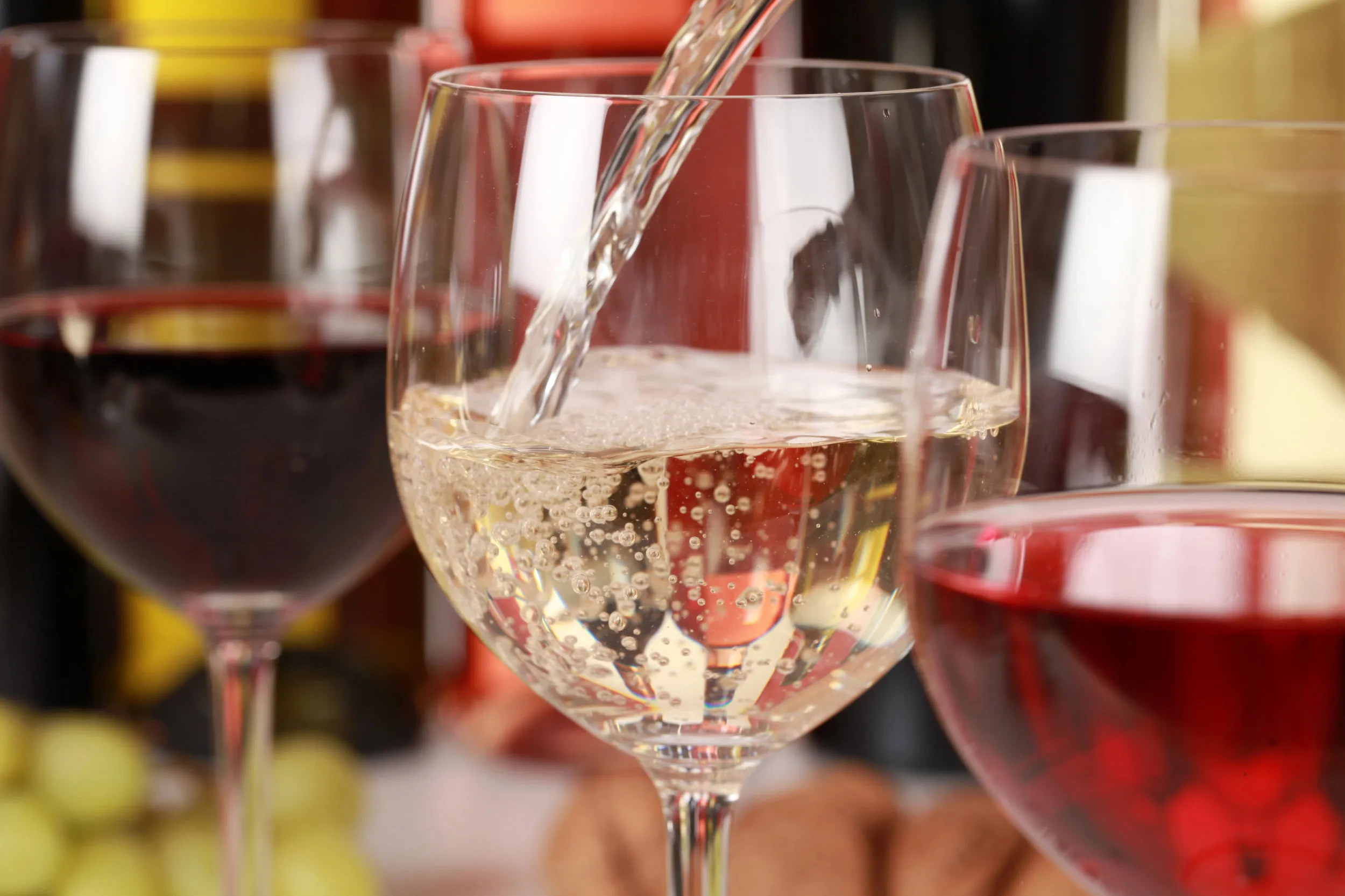White wine poured into a glass, with other glasses and bottles behind