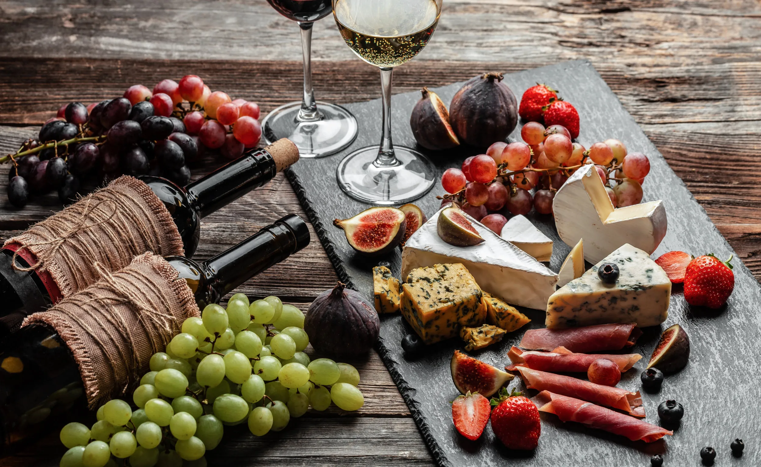 A board of cheese, fruit and charcuterie with two bottles of wine